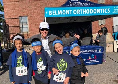 Dr. Melita and young kids standing together in front of Belmont Orthodontics Sponsor Tent